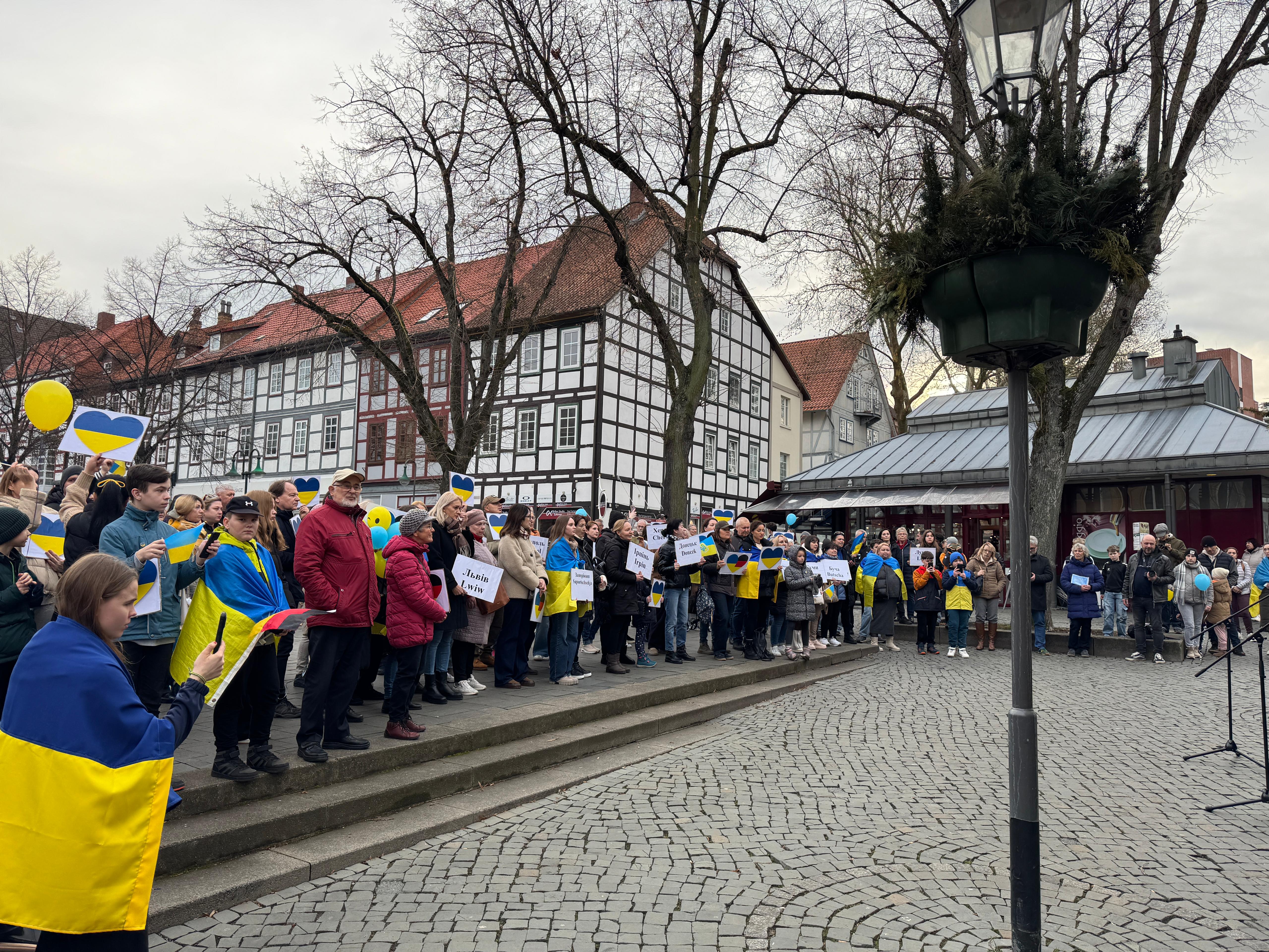 Einige Teilnehmer der Kundgebung stehen auf dem Marktplatz von Northeim und halten blau-gelbe Herzen hoch oder sind in Ukrainefahnen gehüllt.